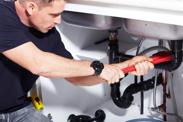 Plumber repairing a pipe under a sink.